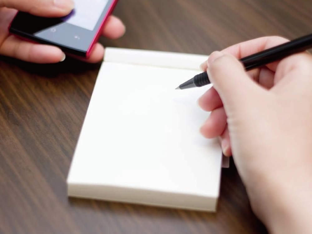 左手拿手機右手拿筆預備抄寫資料的意象照片