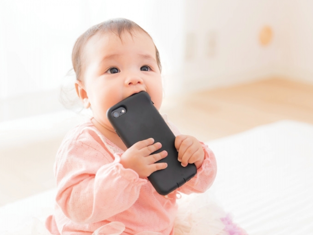 嬰兒咬著手機外殼象徵接觸3C產品的照片