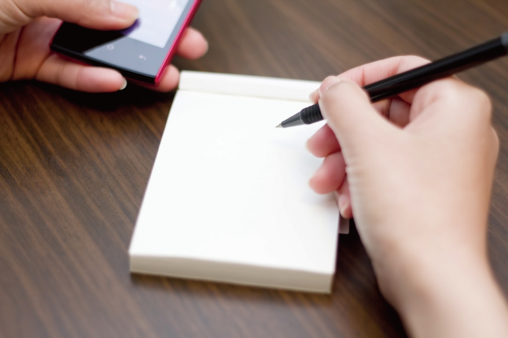 手持手機並預備抄寫資料的意象圖