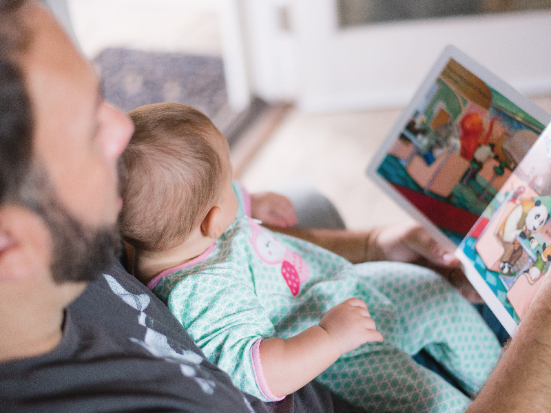 大人抱嬰兒一起閱讀兒童讀物照片